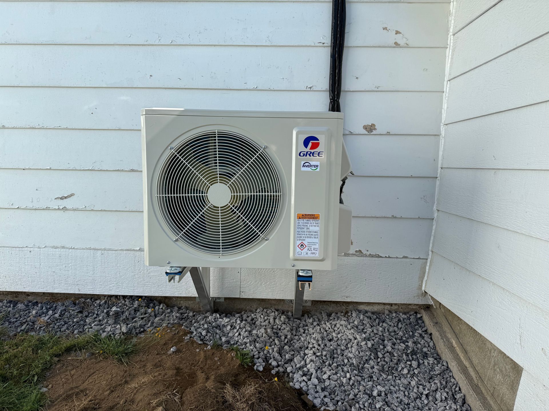 Unité de climatisation Gree montée sur l'extérieur d'une maison blanche avec un sol en gravier.