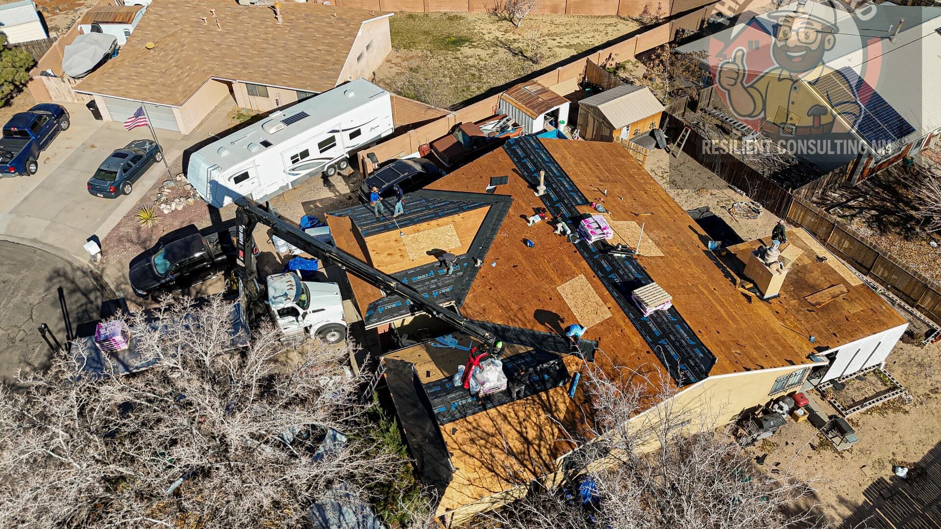 Aerial view of storm-damaged homes with torn roofs, debris, and damaged vehicles scattered around.