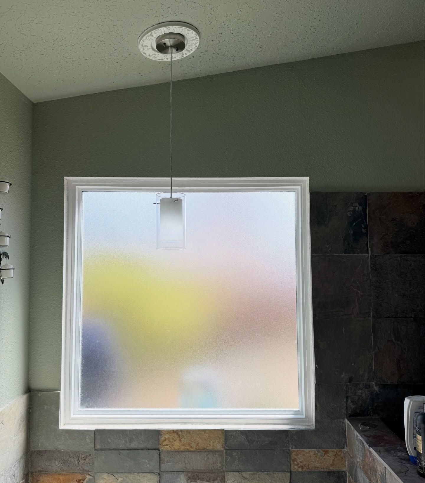 Small frosted window above stone ledge in a green-walled bathroom with a hanging light fixture
