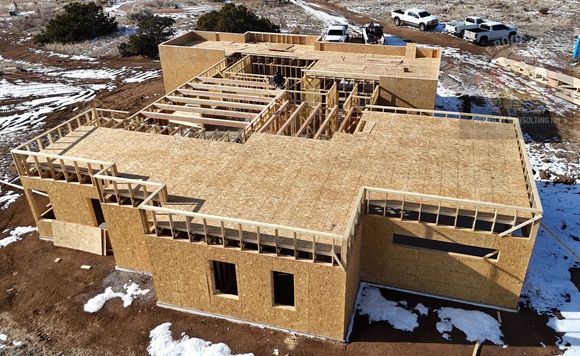 Wood-framed house under construction with roof trusses and plywood sheathing in a snowy lot.