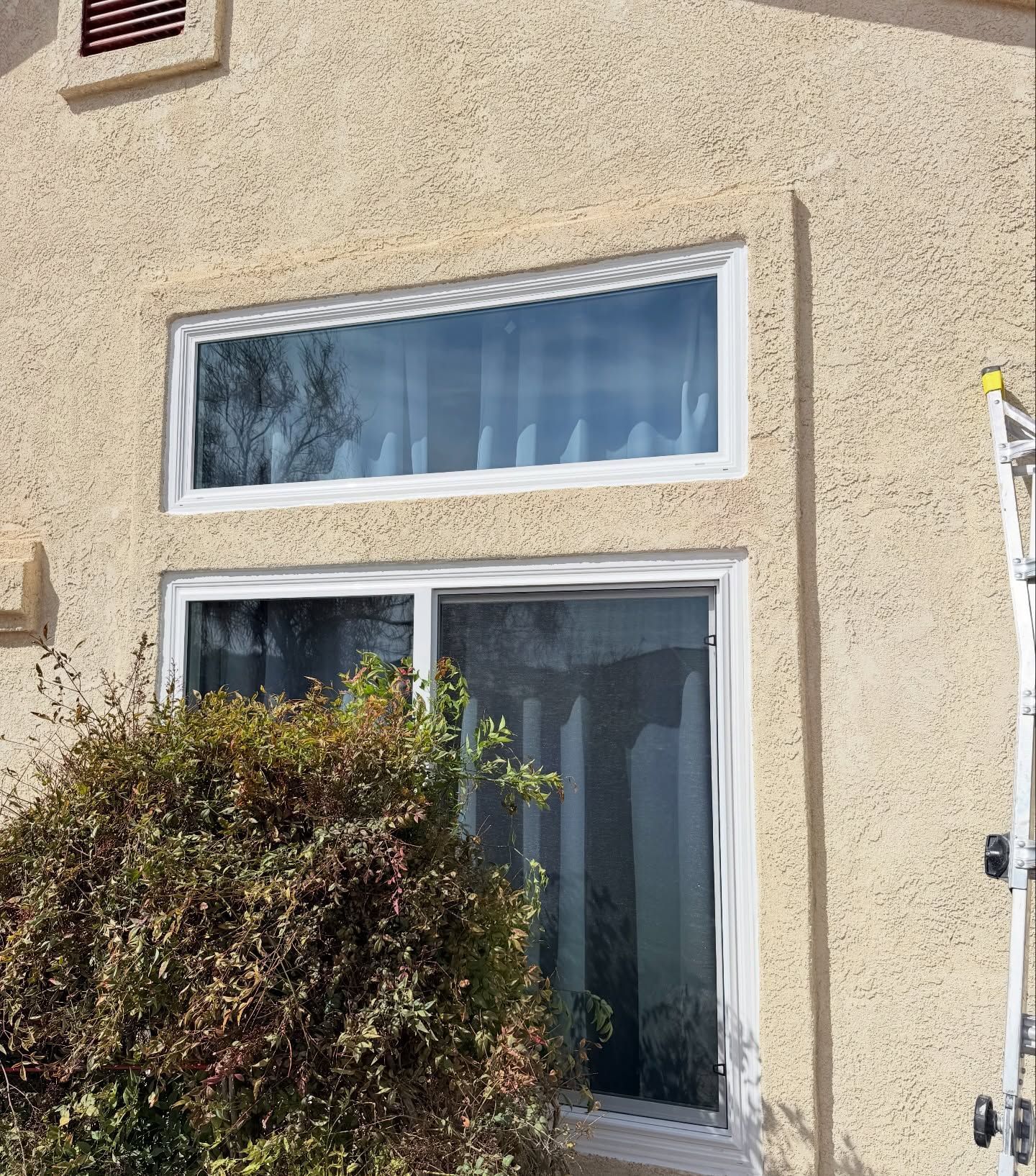 Stucco house exterior with a white-framed window, sliding glass door, and bush in front