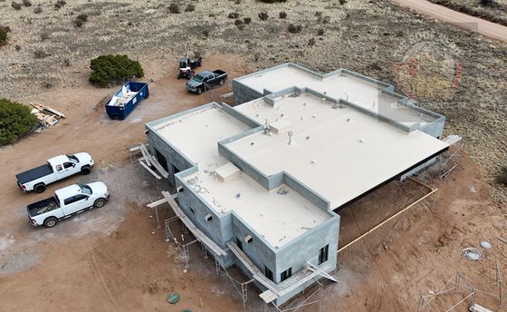 Aerial view of a large white house under construction with several pickup trucks on a dirt lot.
