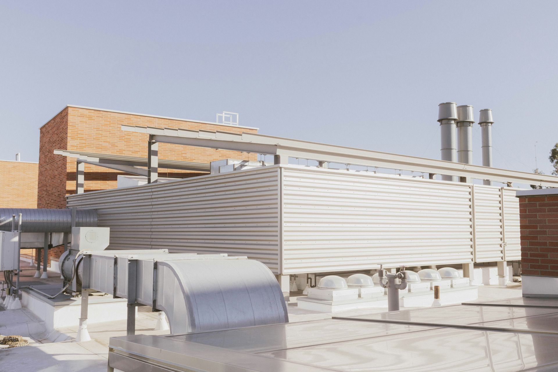 Rooftop HVAC units and ductwork beside a brick building under a clear sky