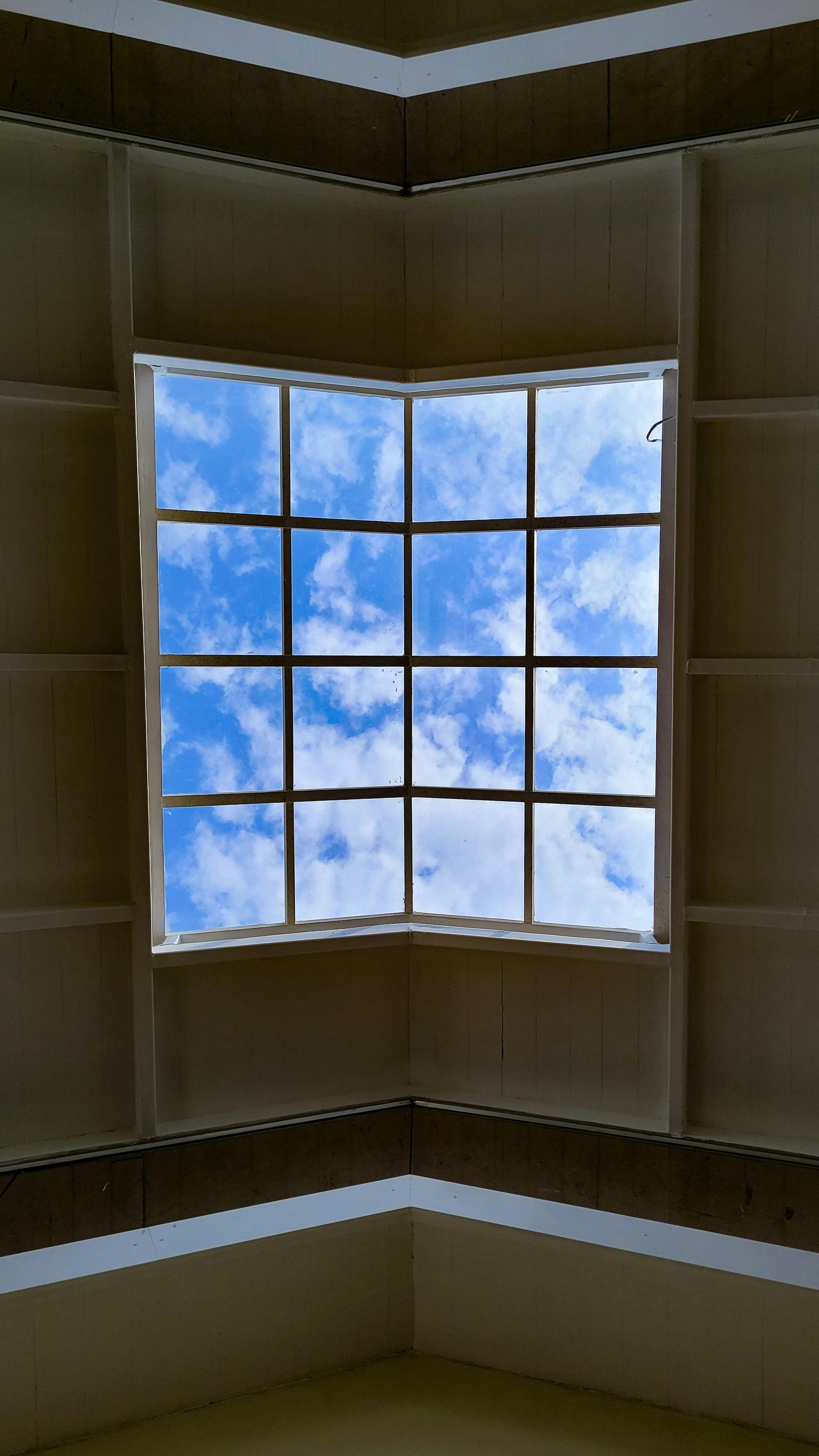 Curved skylight window with blue sky and clouds, framed by beige interior walls.
