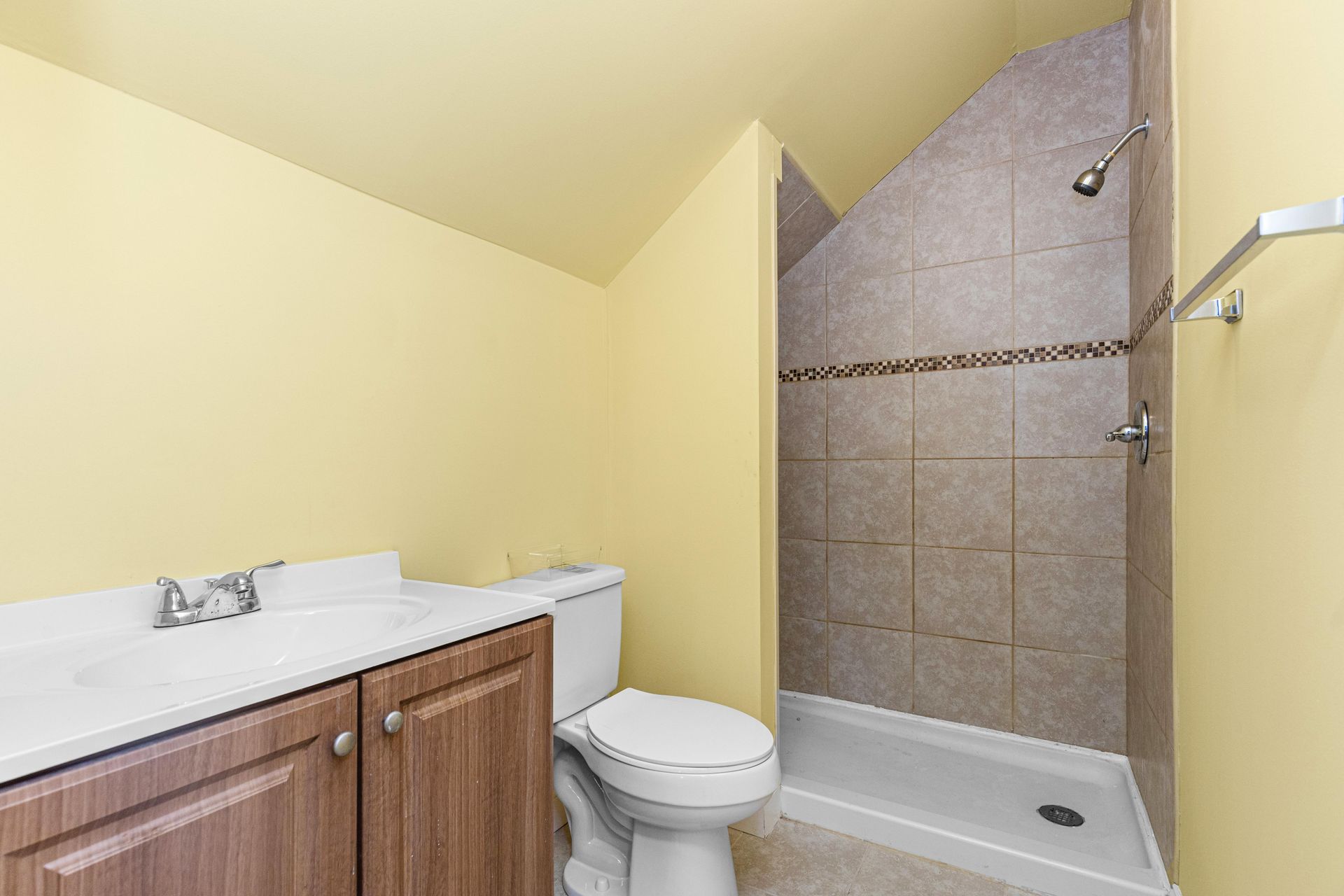 Small bathroom with vanity, toilet, and tiled shower stall in yellow walls.