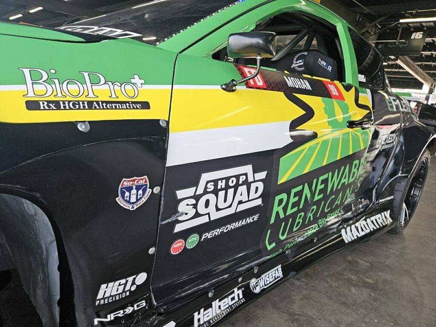 Green and black race car with sponsor logos, parked indoors.