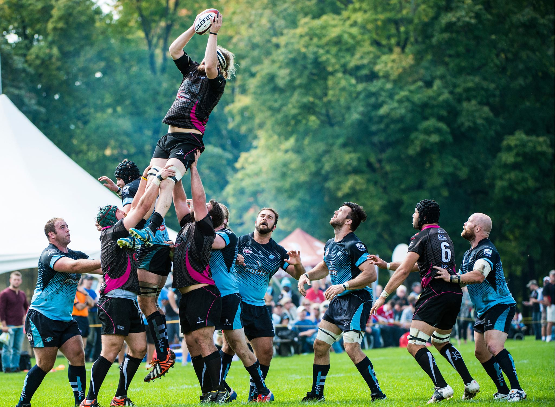 Rugby players in blue and black kits perform a lineout, lifting a teammate high into the air to catch the ball.