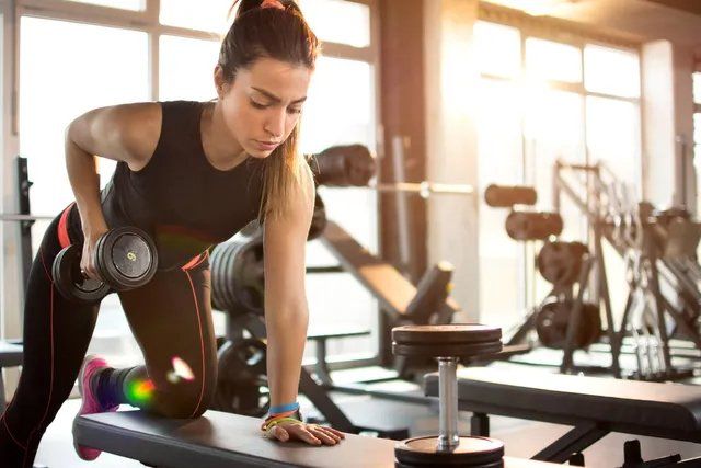 A woman is lifting a dumbbell on a bench in a gym.