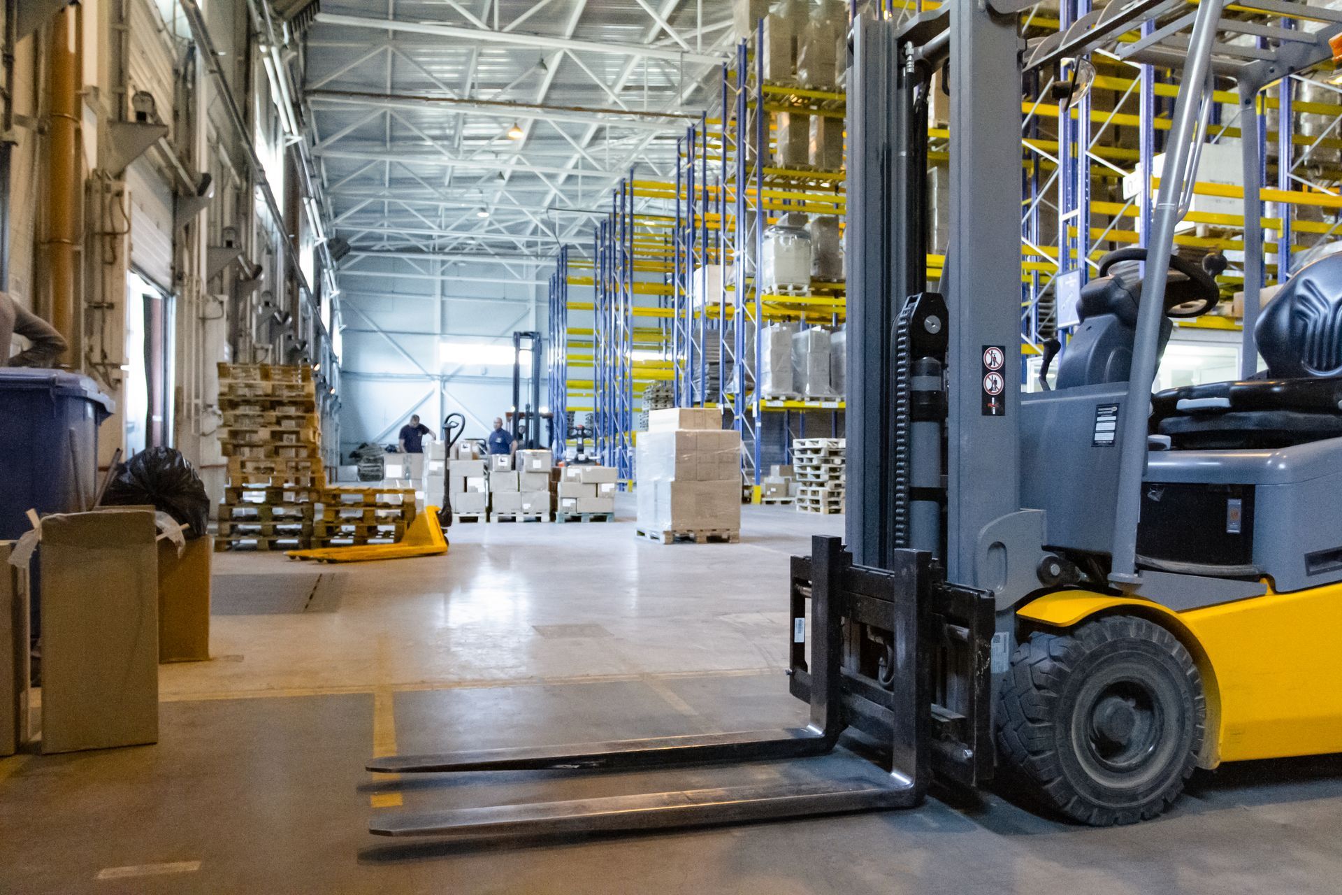 Warehouse interior with a yellow forklift carrying pallets along a wide aisle