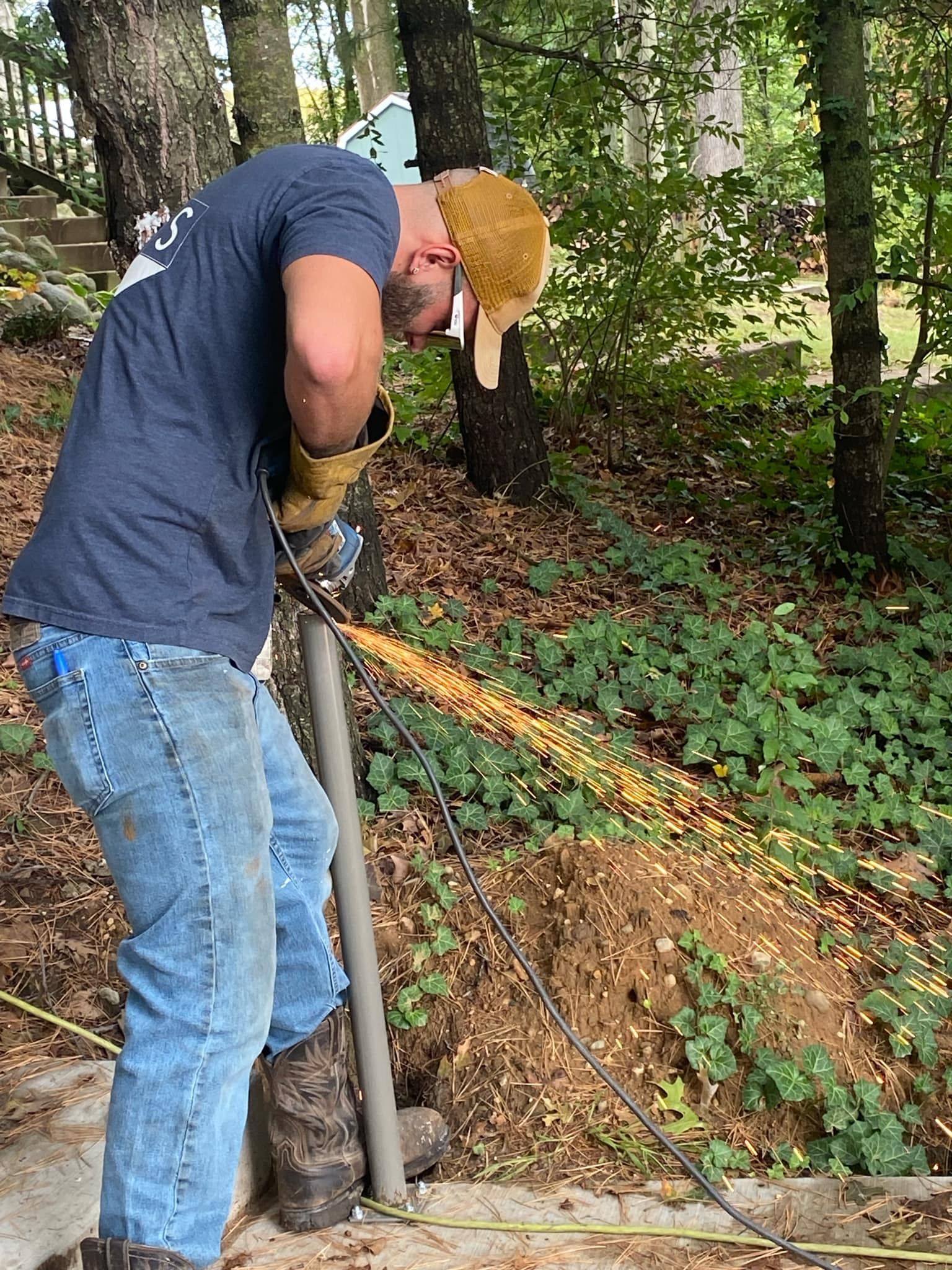 Person welding metal post outdoors, sparks flying.