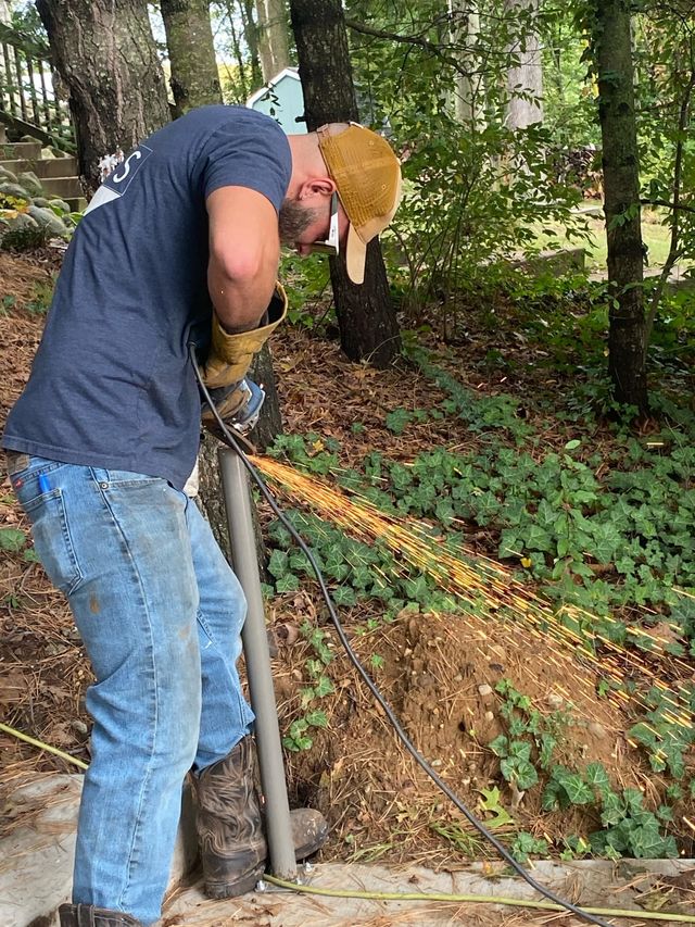 Person welding metal post outdoors, sparks flying.