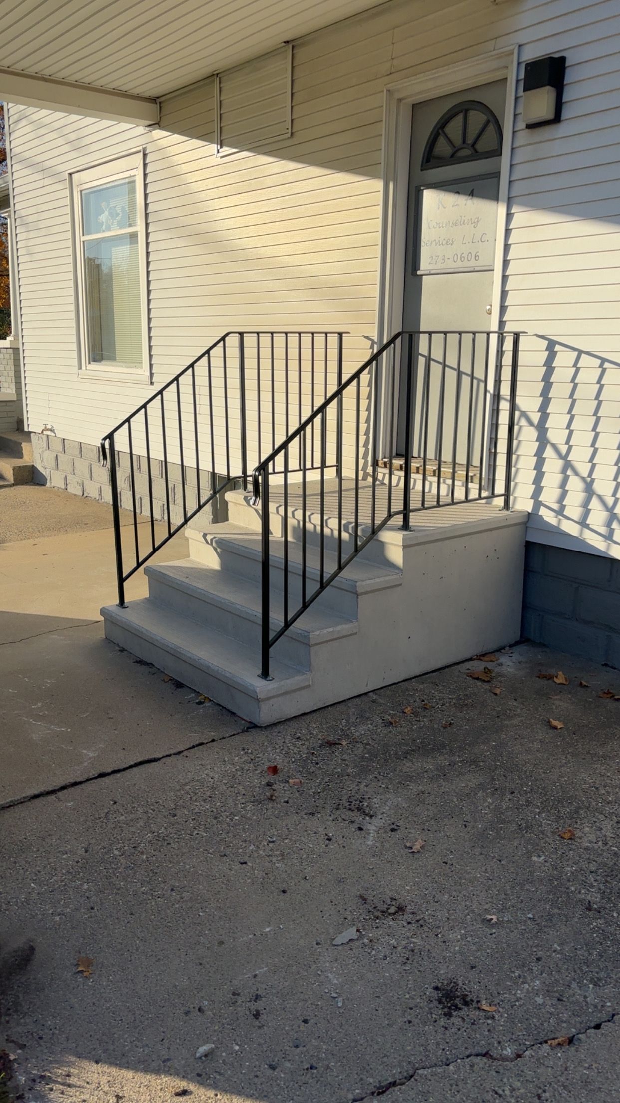 Concrete steps with black metal railing leading to a white building's front door.
