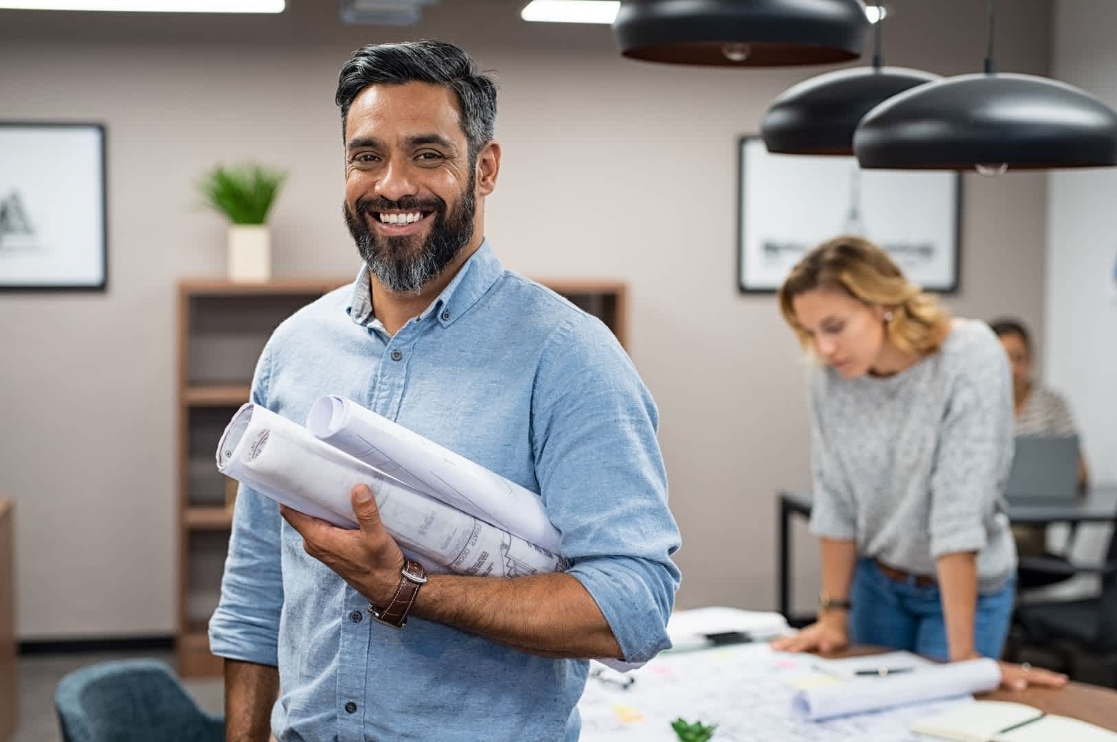 Man holding blueprints smiles in office setting. Man holding blueprints smiles in office setting.