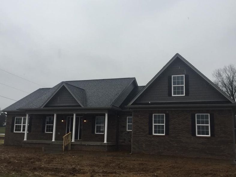 A newly built dark-brick house with a gray roof and a front porch under a cloudy sky.