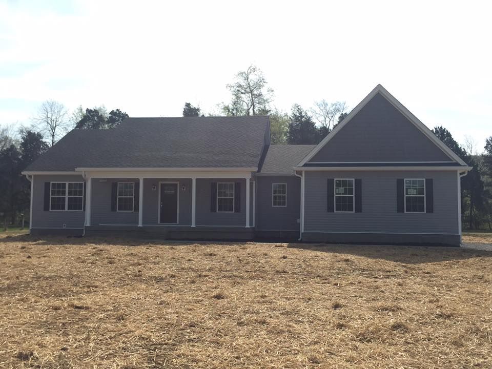 A newly constructed gray, single-story suburban house with a covered front porch, set on a plot of cleared land.