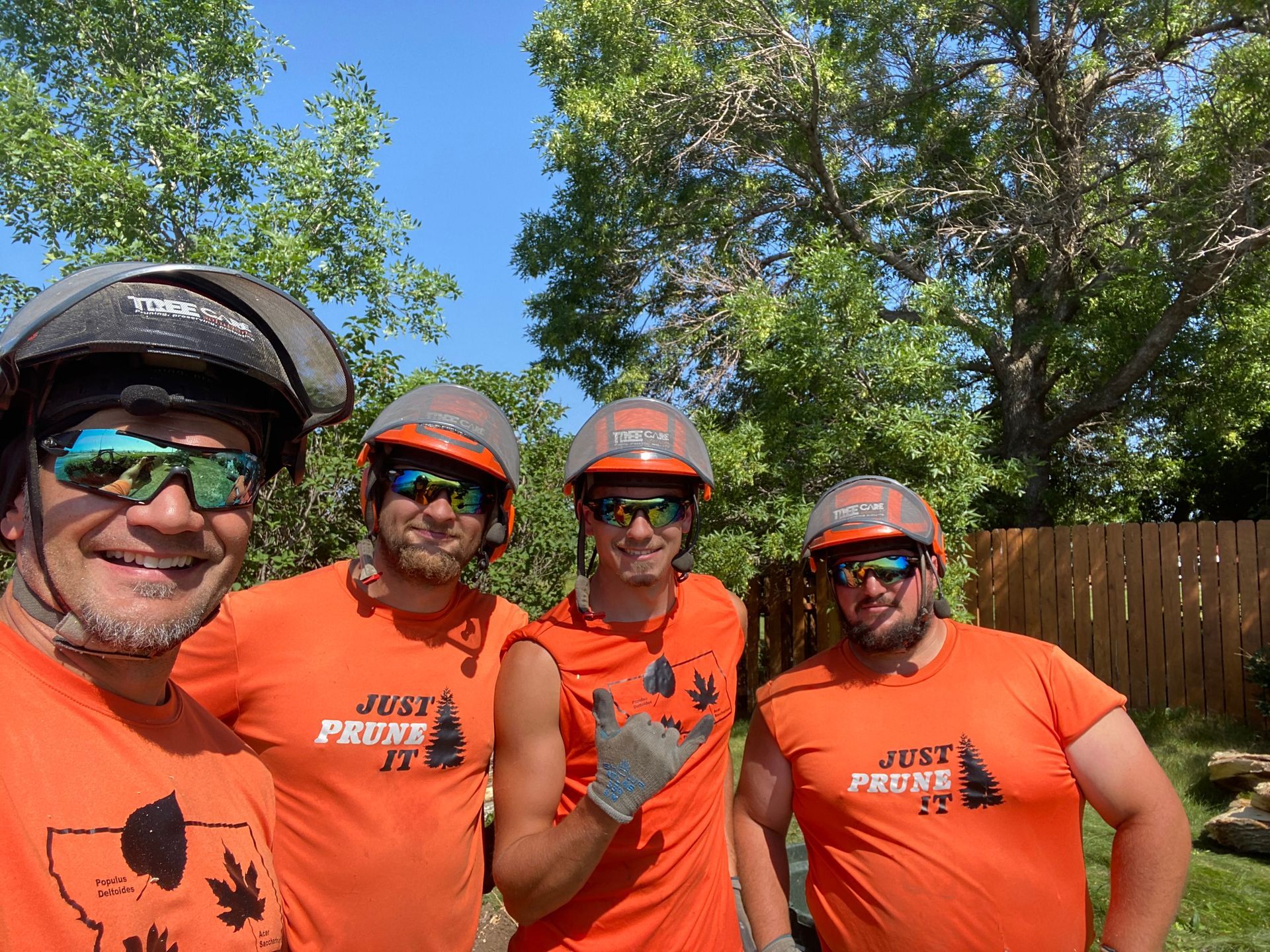 Four cyclists in orange shirts and helmets posing outdoors in bright sunlight.