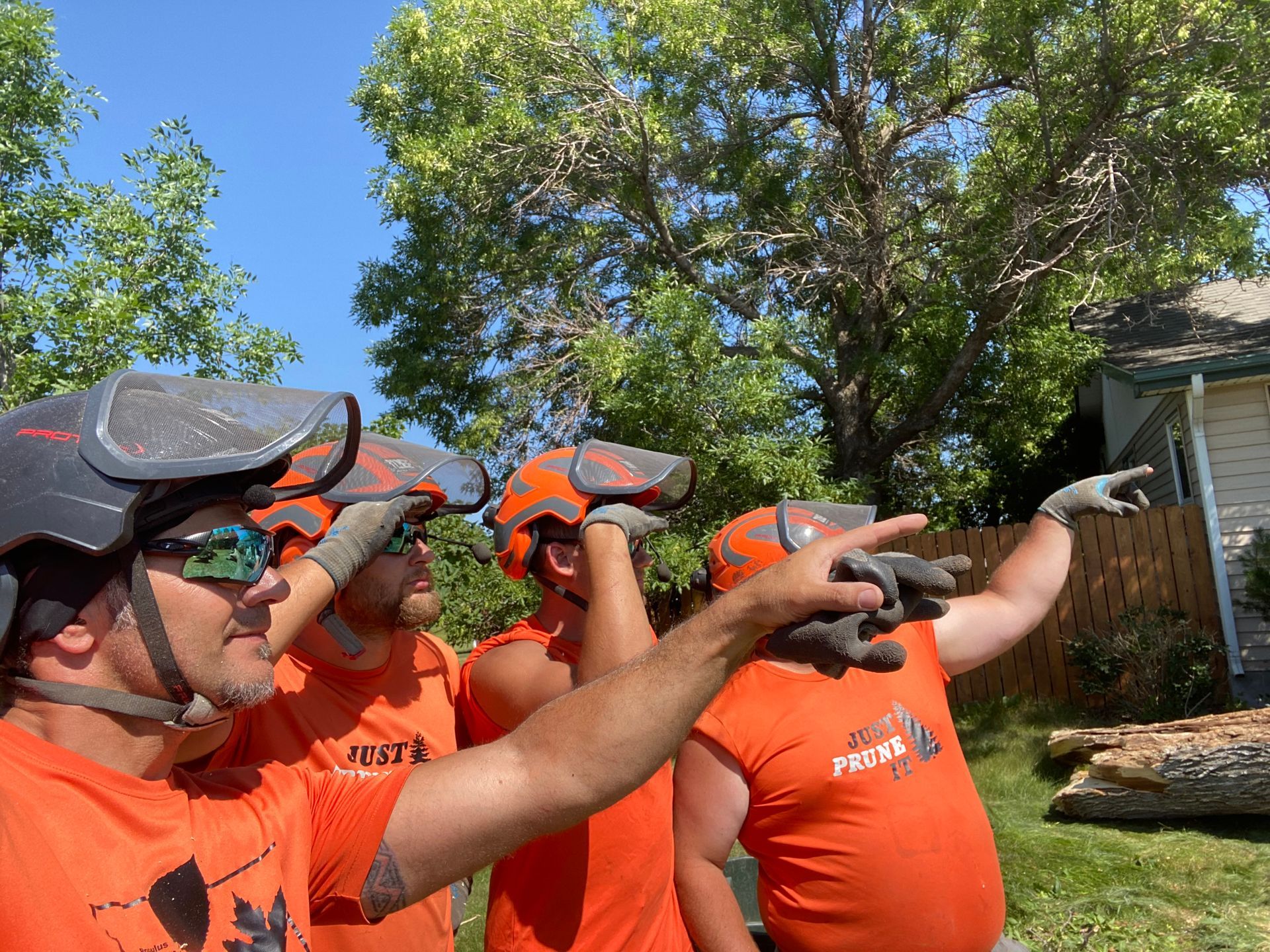 Three people in orange shirts and ear protection aiming paintball markers outdoors.