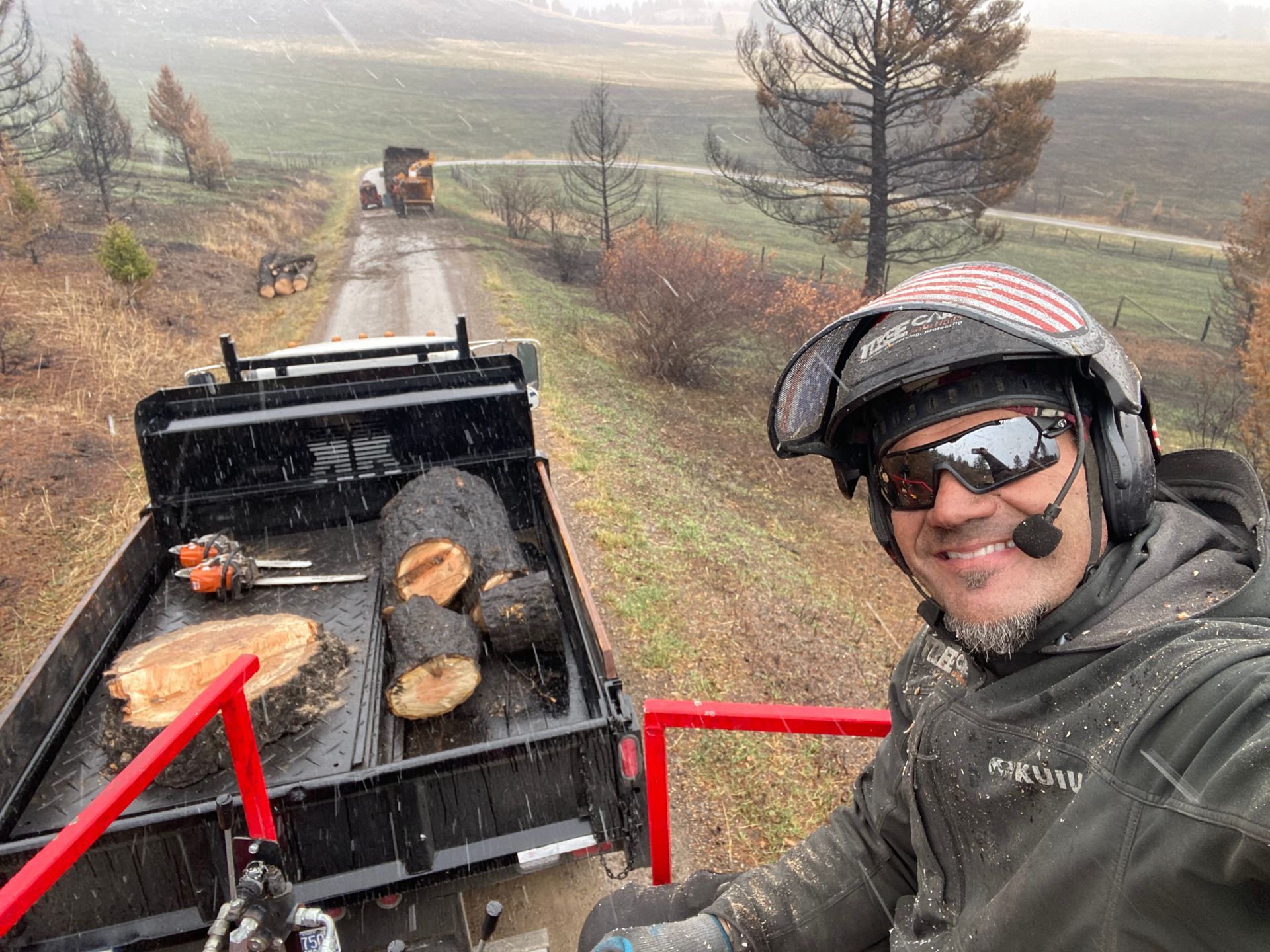 Smiling rider on a quad, with black cargo bed carrying firewood, on a muddy trail in a foggy countryside