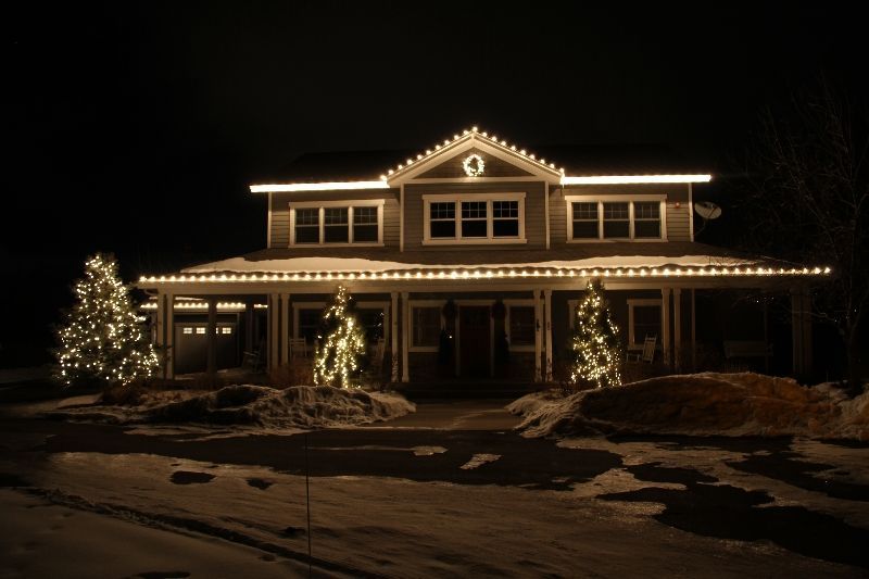 Snowy house decorated with warm white Christmas lights at night
