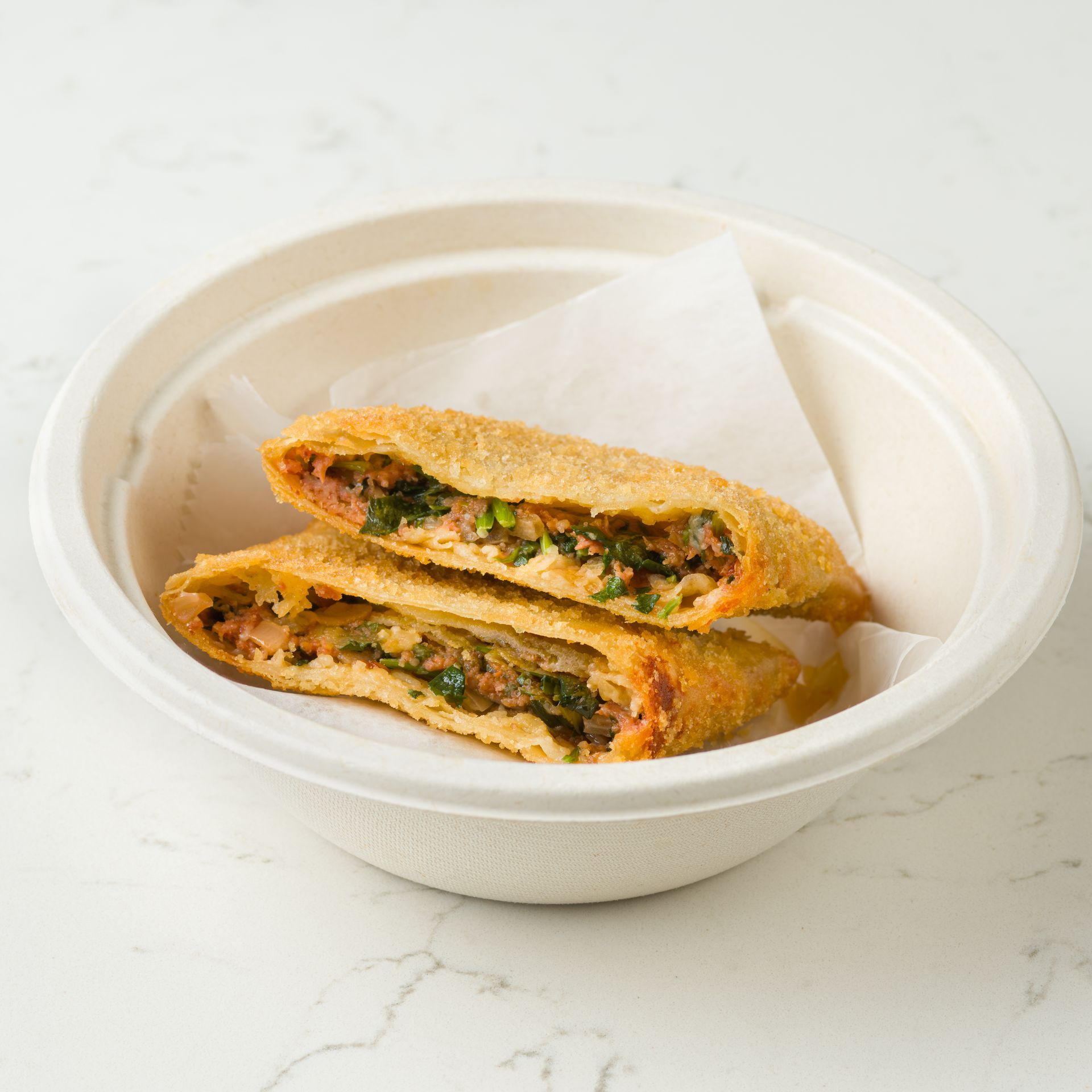 Two halves of a toasted stuffed pastry in a white bowl on a light marble surface