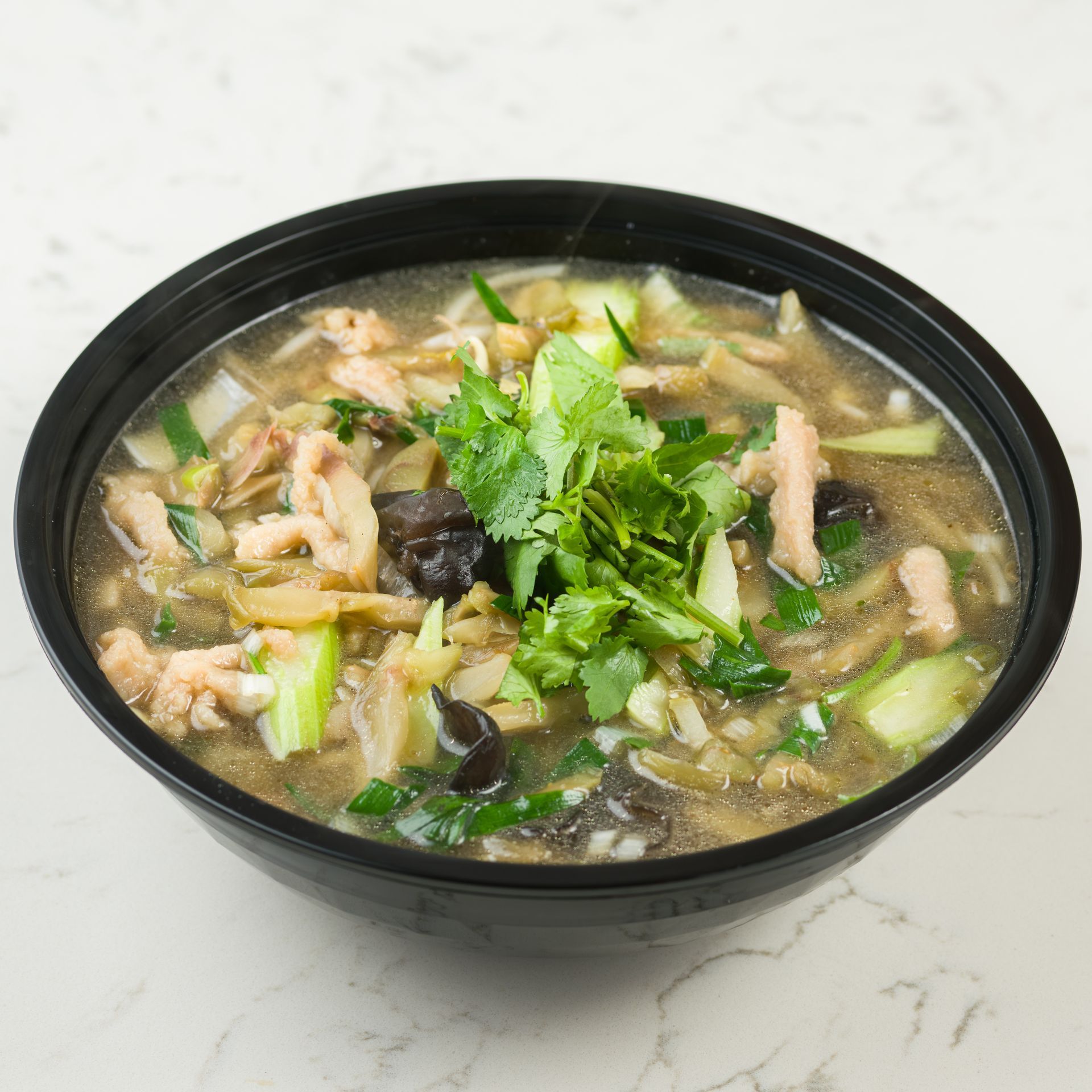 Black bowl of noodle soup topped with cilantro and vegetables on a light surface