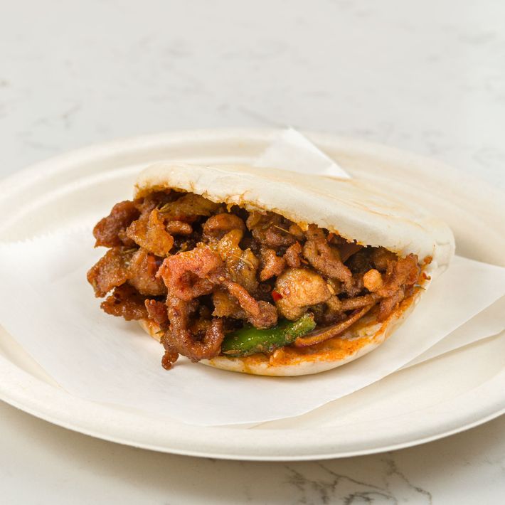 A taco with grilled meat and peppers in a white paper wrapper on a white plate