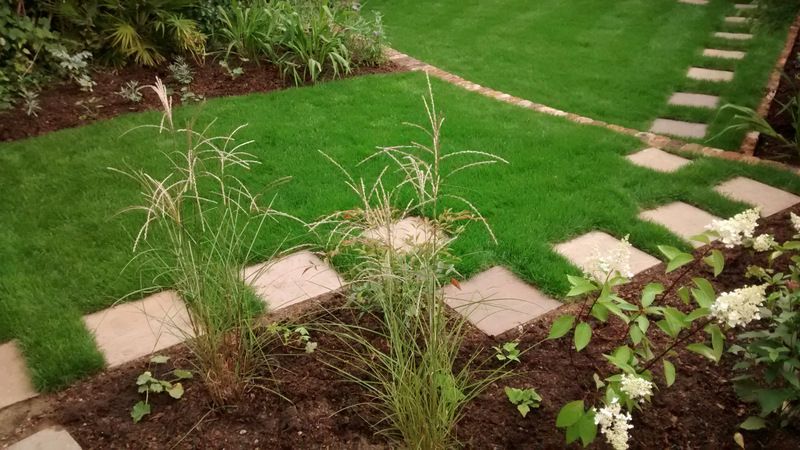 Path along the edge of the lawn with a bed beside planted with grasses and perennials