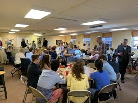 People seated in a meeting room, talking around tables during a group discussion.