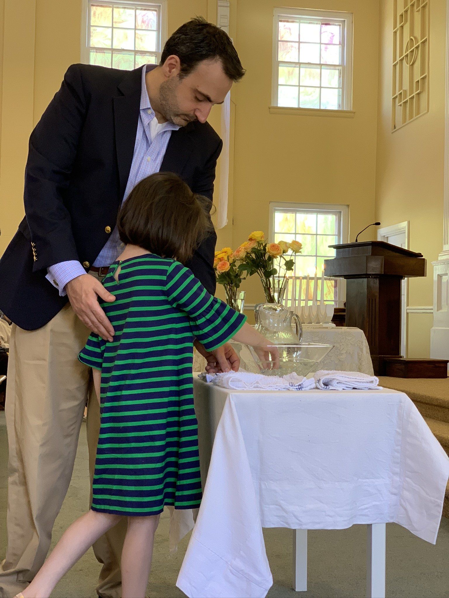 Man in a dark jacket guiding a child beside a set table in a bright room