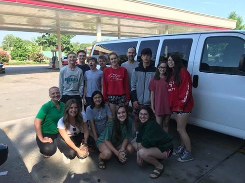 Group of people posing outside a gas station beside a white van, smiling at the camera.
