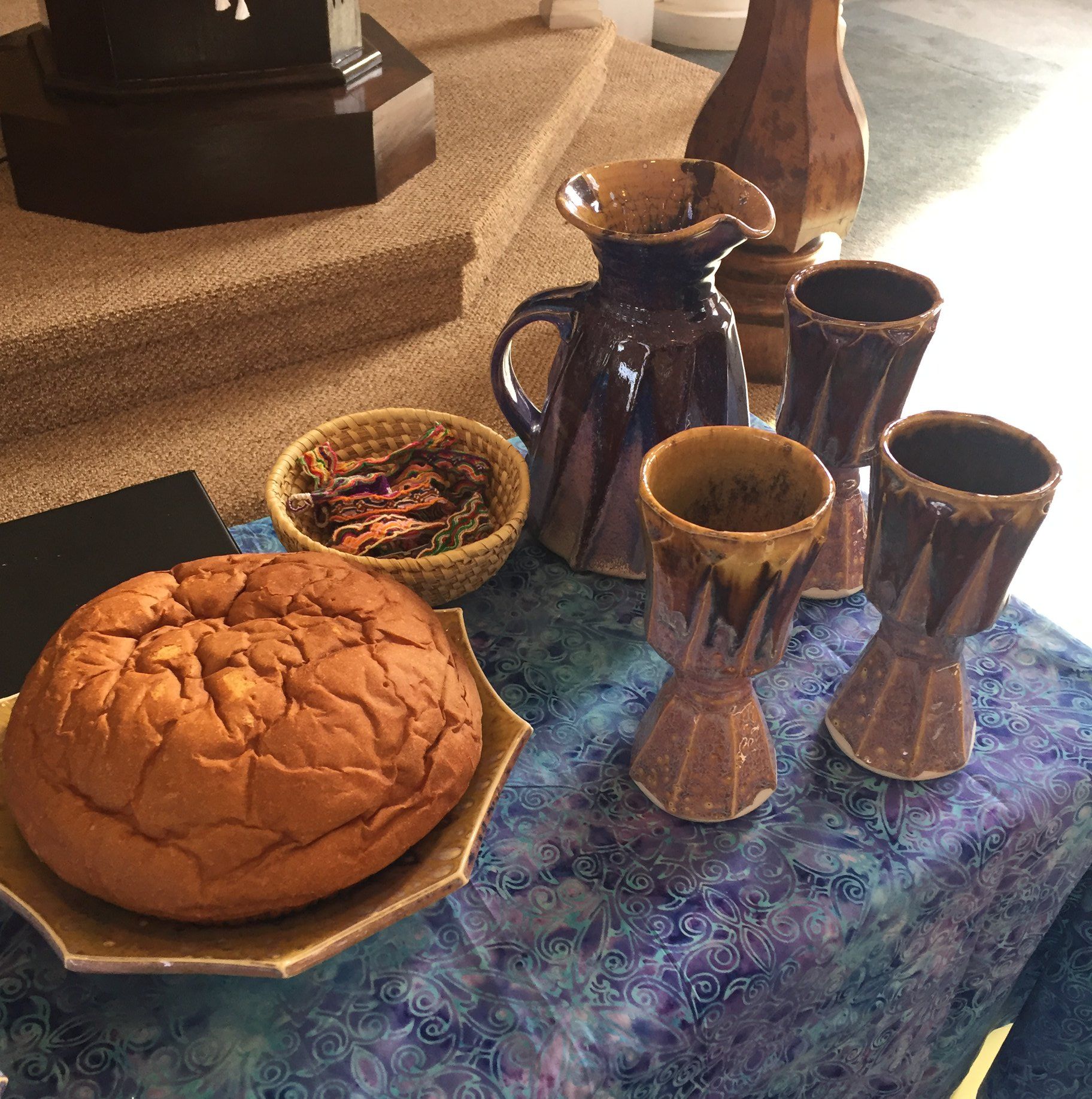 A loaf of bread and pottery mugs on a table with a blue patterned cloth.