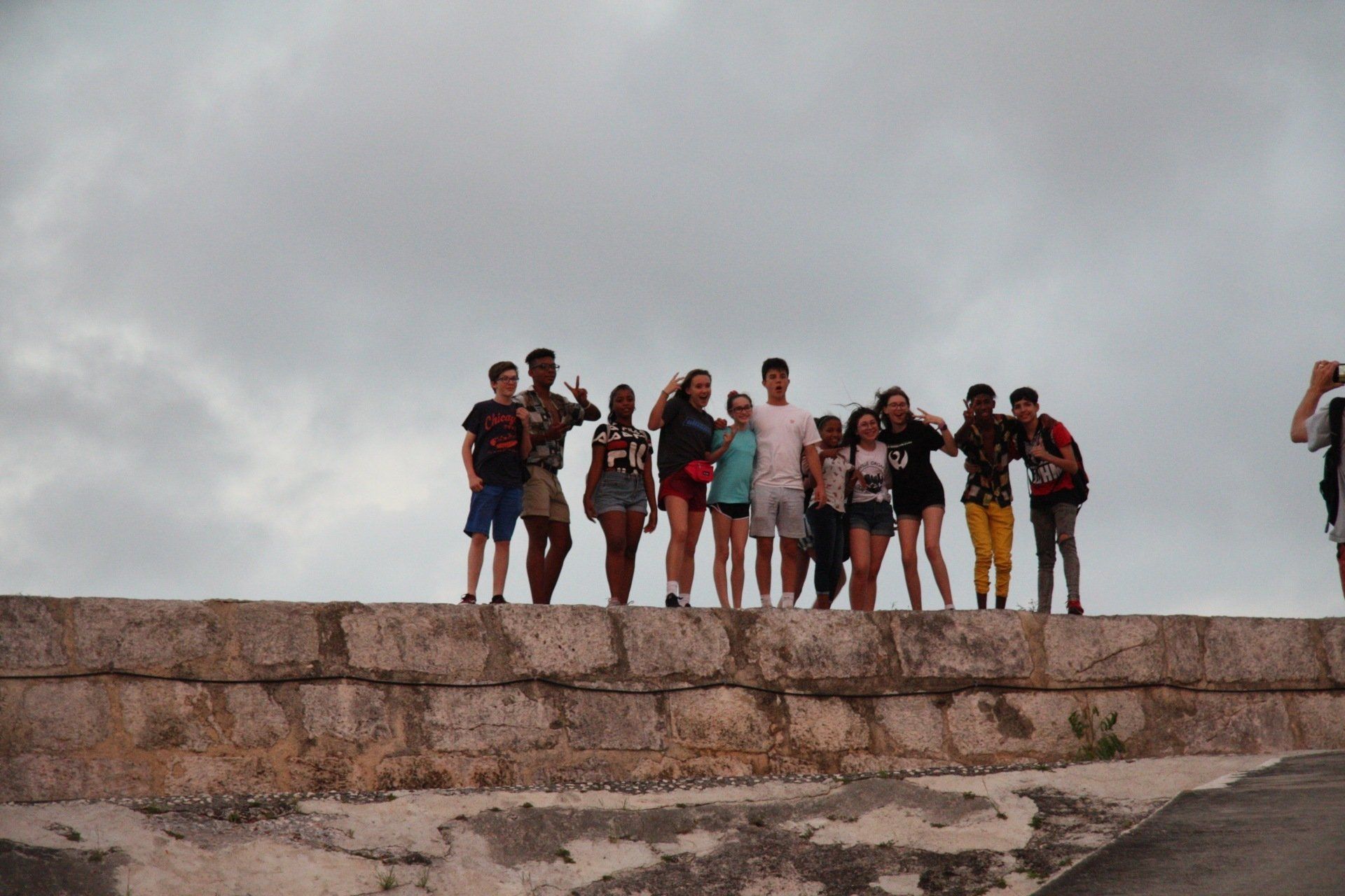 Group of people standing on a stone wall under a cloudy sky, posing for a photo