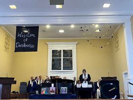 Church stage with people seated and standing beneath a “Worship of Deliverance” banner