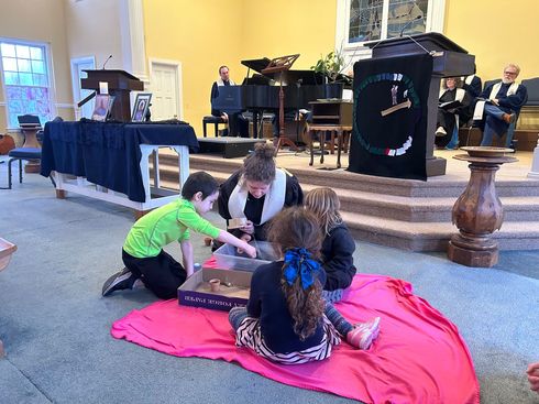 Children playing with a board game on a red blanket in a church sanctuary near the stage