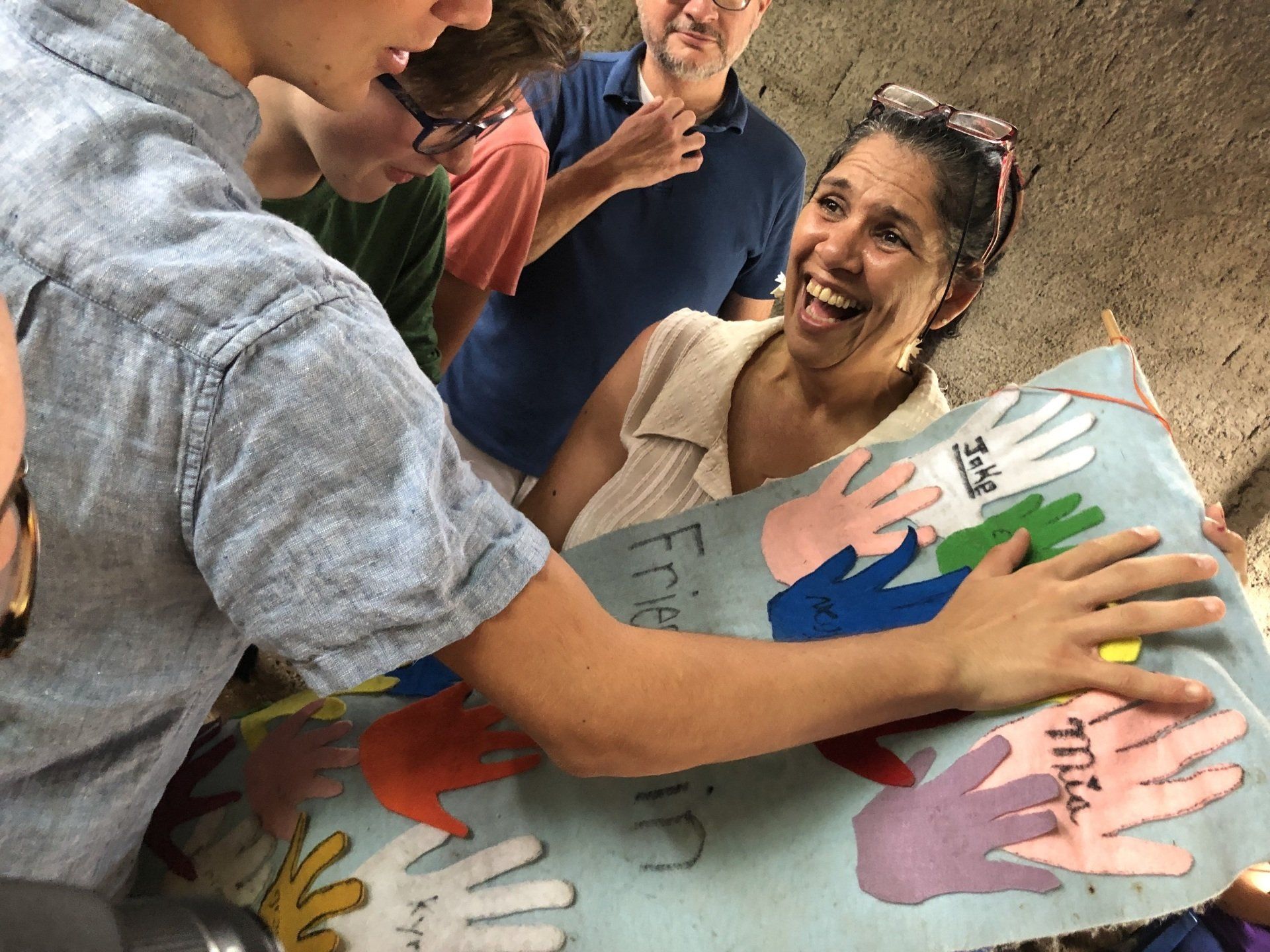 People smiling as they wrap a colorful handprint quilt around someone outdoors