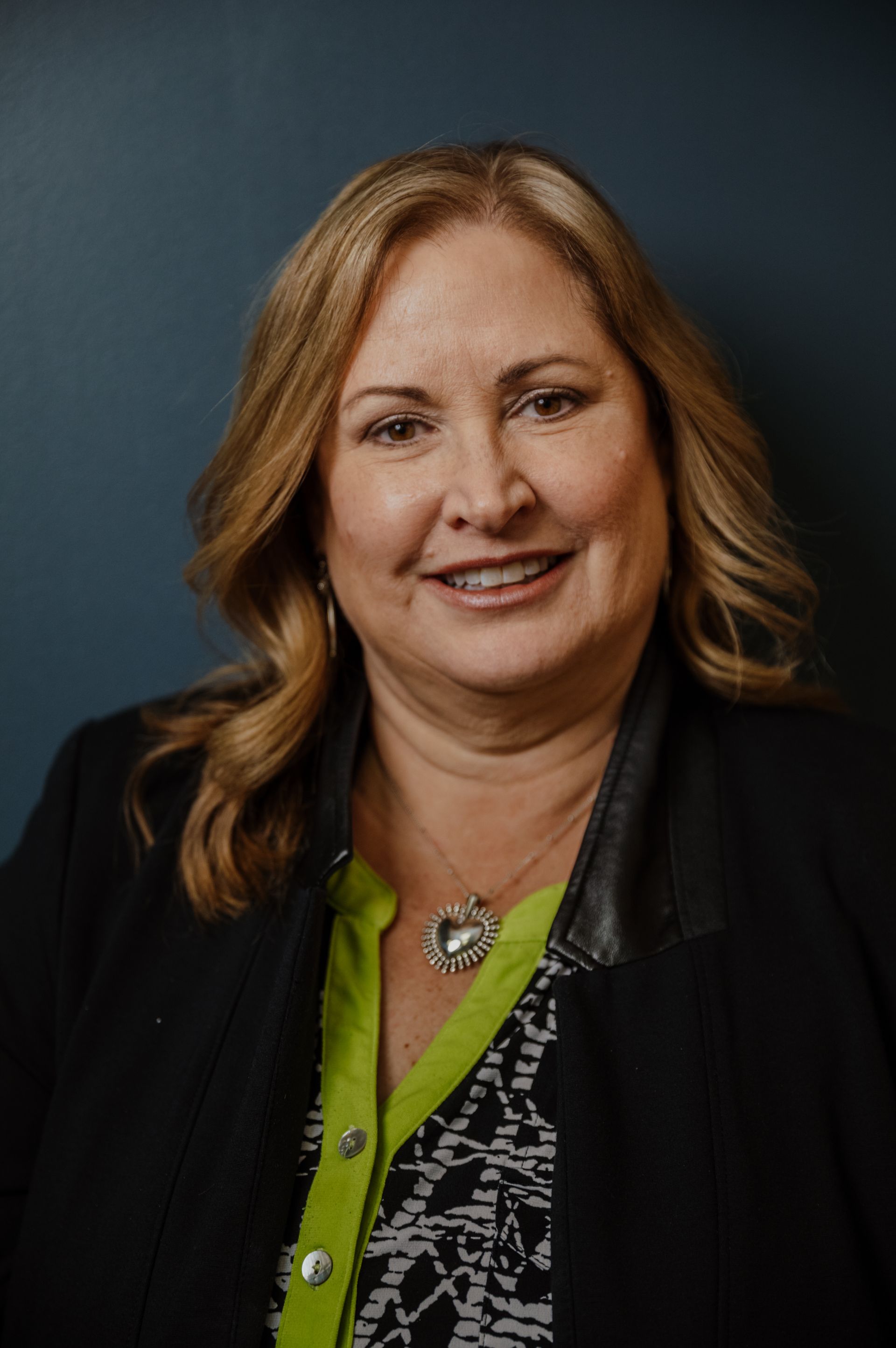 A woman wearing a black jacket and a green shirt is smiling for the camera.