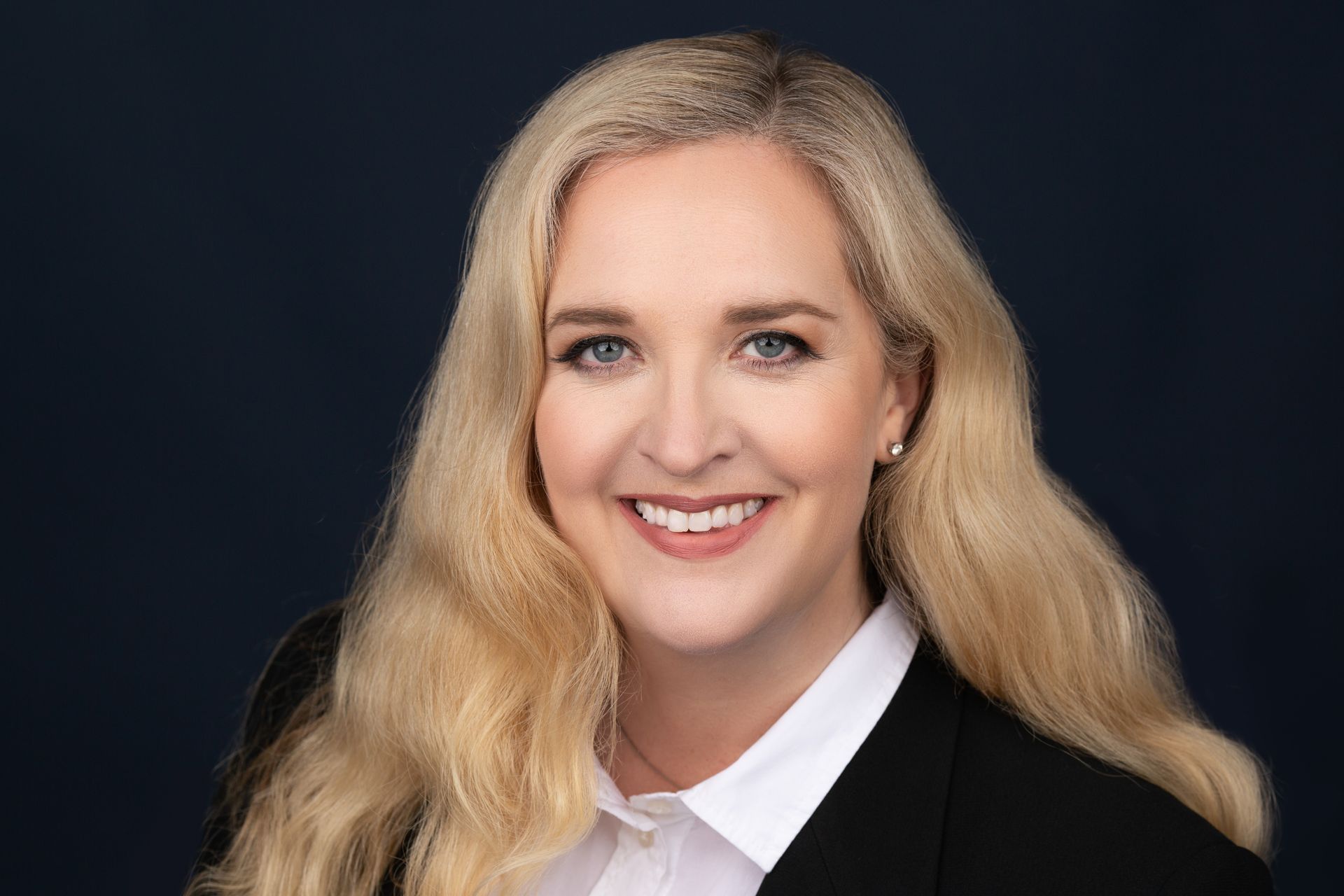 A woman in a suit and white shirt is smiling for the camera.