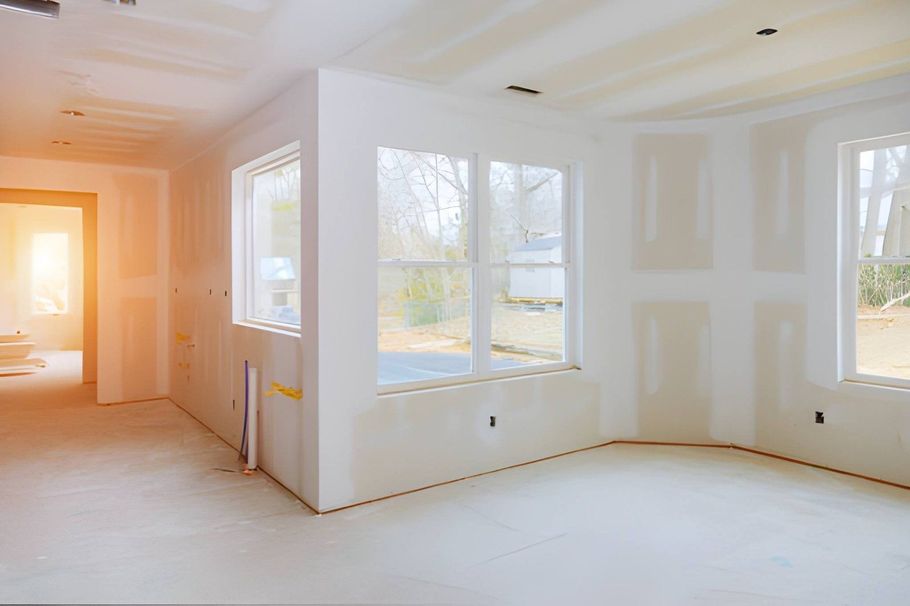 Bright unfinished room with white walls, large windows, and sunlight on the floor