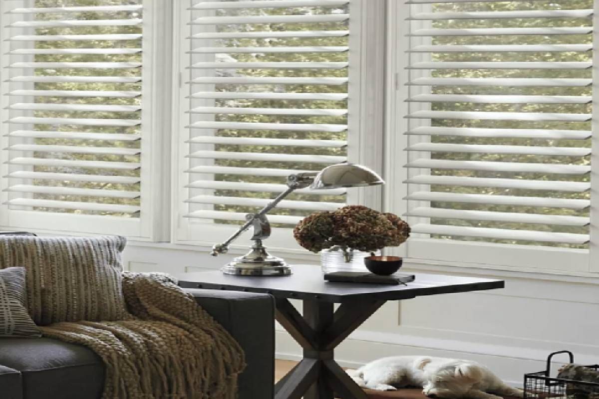 A table and sofa in a living room with large windows covered by NewStyle® Composite Shutters near San Diego, California