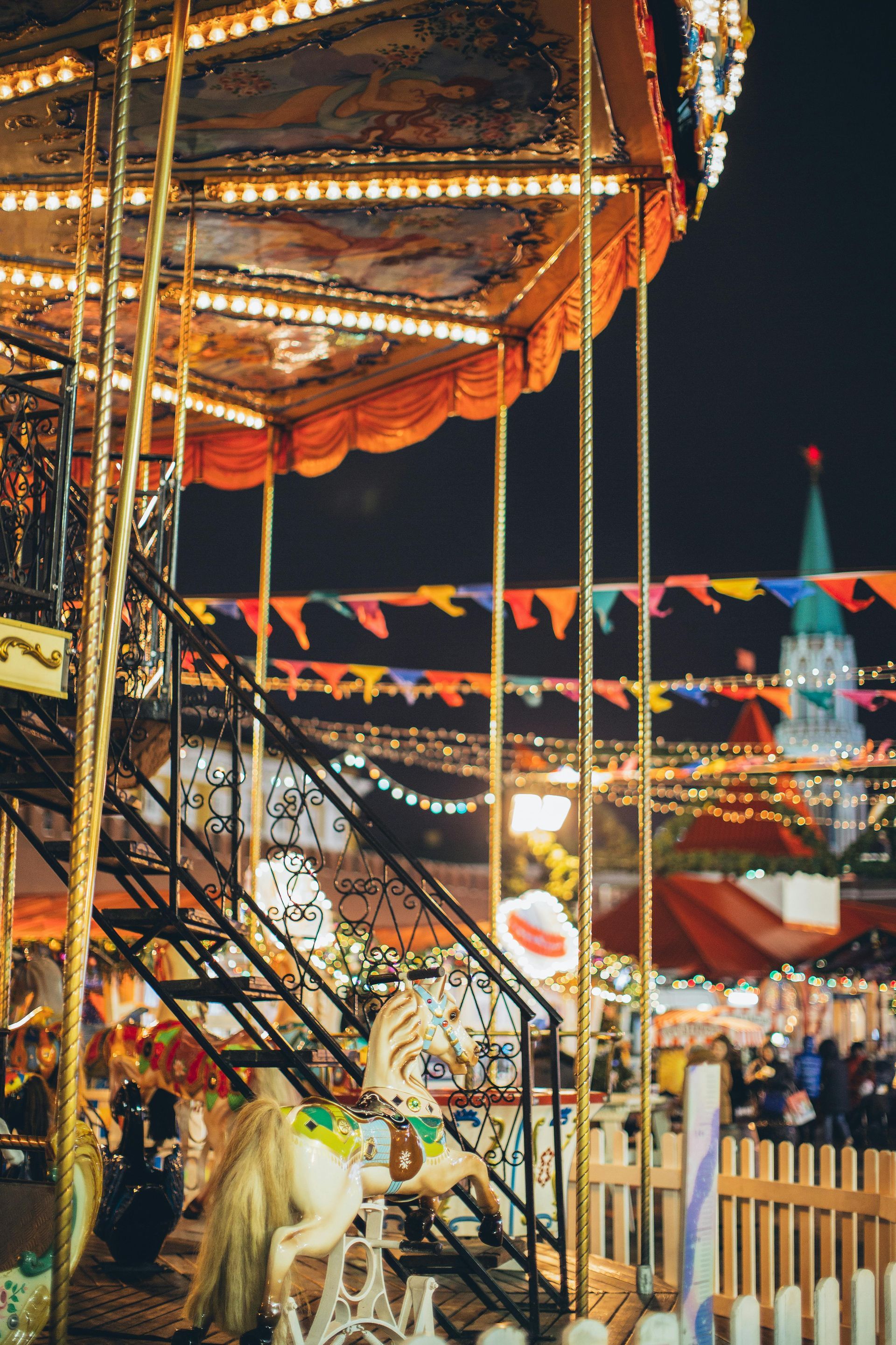 A brightly lit carousel at night, featuring decorative gold poles and strings of colorful pennant flags against a dark sky.