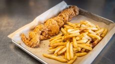 Fried fish and French fries served on parchment in a metal tray