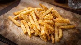 Golden French fries piled on brown parchment paper in a tray