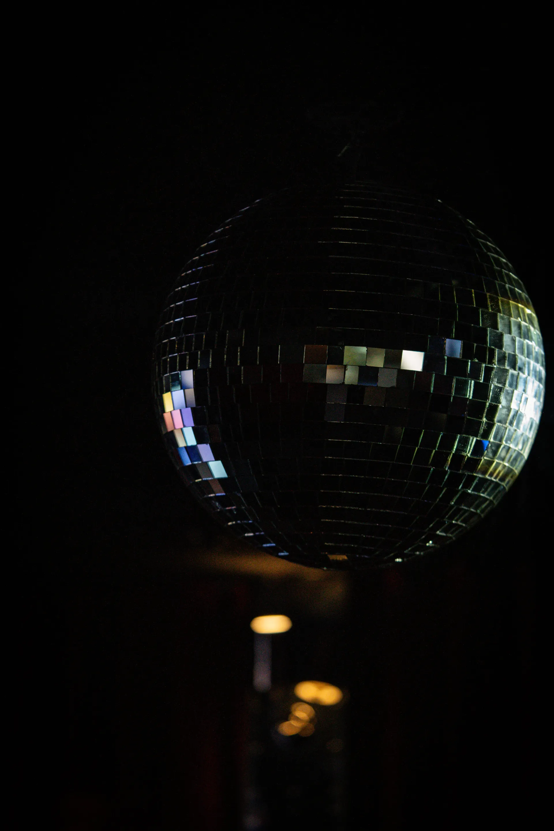 Una bola de discoteca con espejos colgada en una habitación oscura con tenues reflejos de colores.