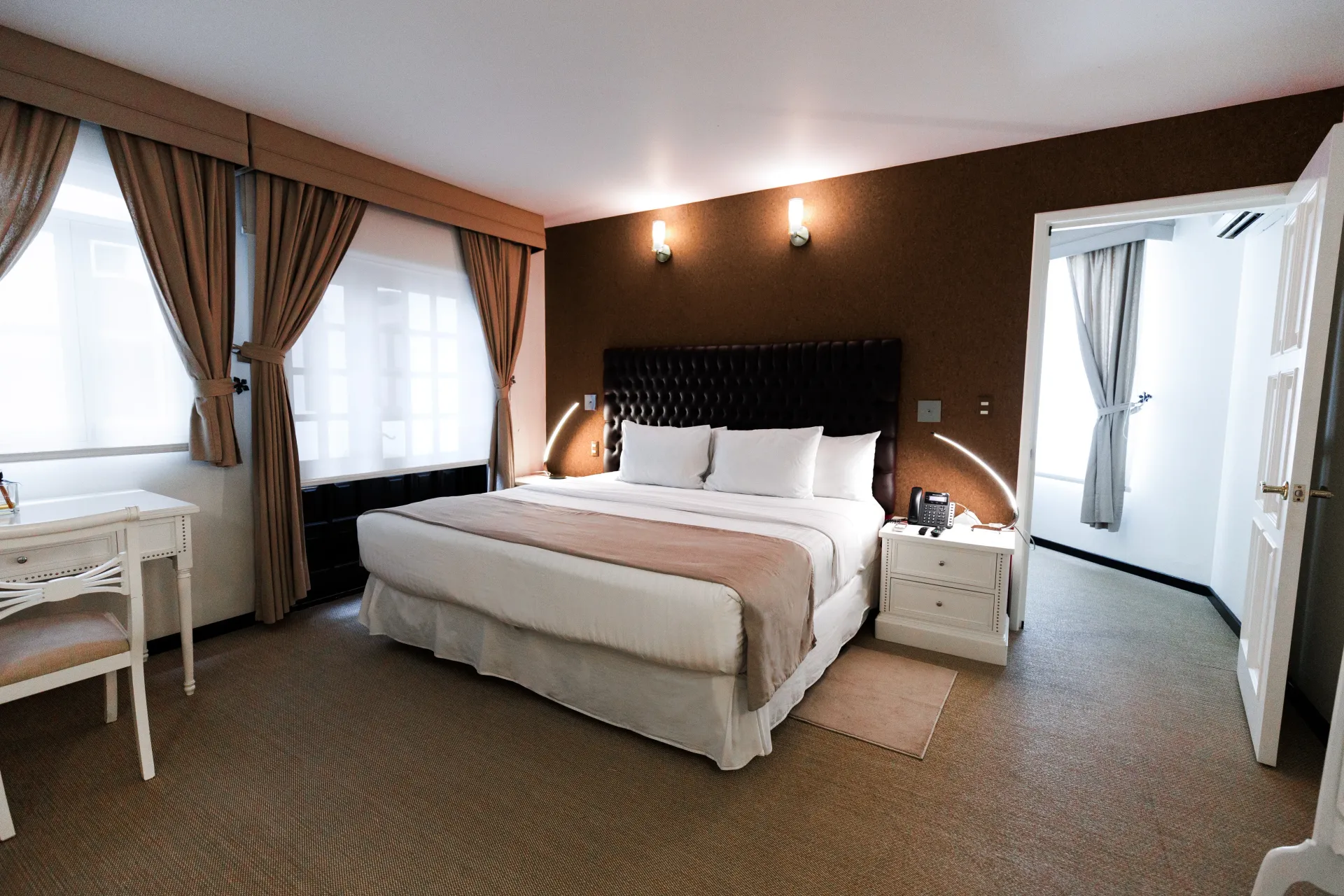 Habitación de hotel luminosa con cama king size, paredes marrones, alfombra estampada, escritorio blanco .