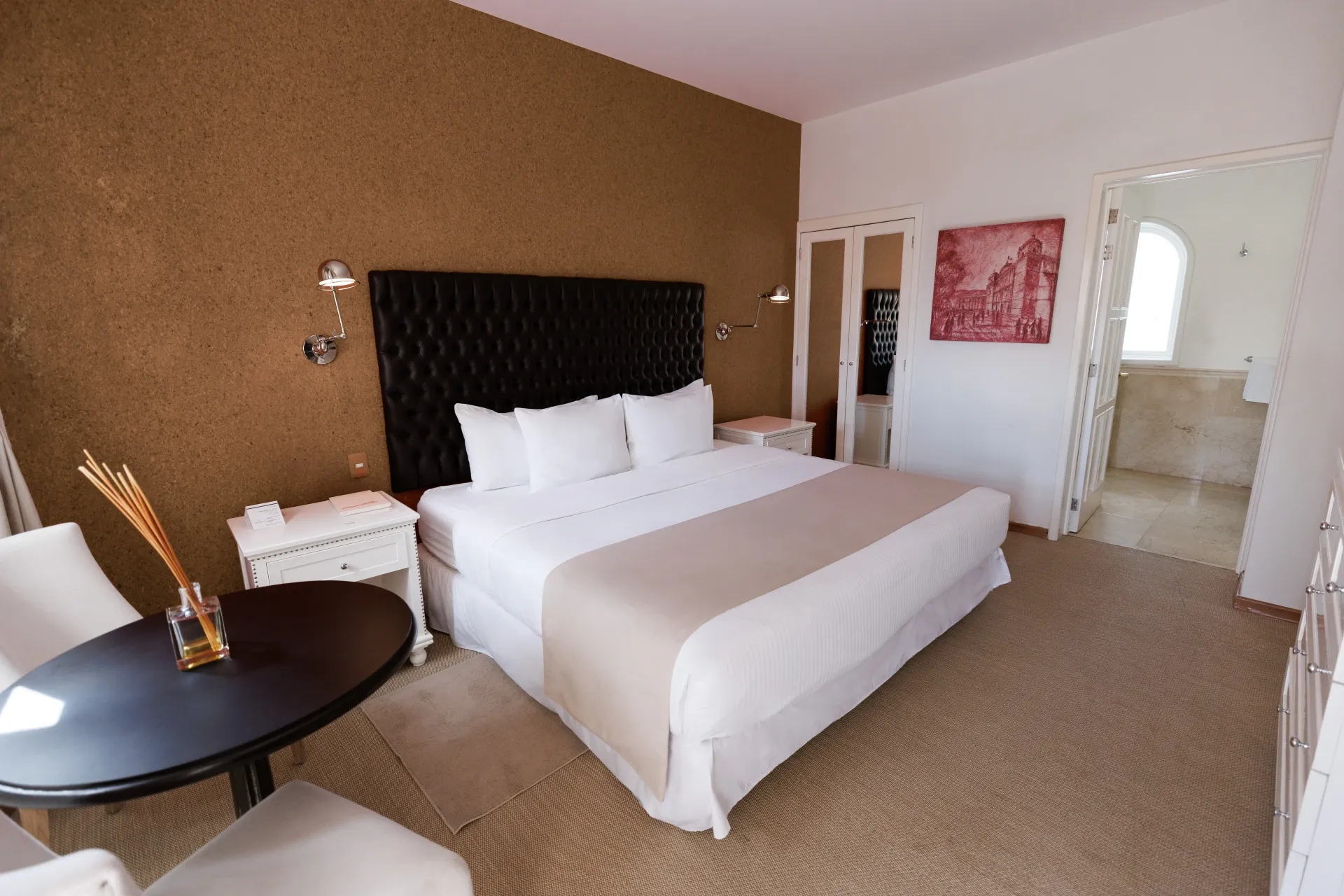 Habitación de hotel moderna con cama king size, paredes estampadas, ropa de cama blanca y una pequeña mesa redonda.