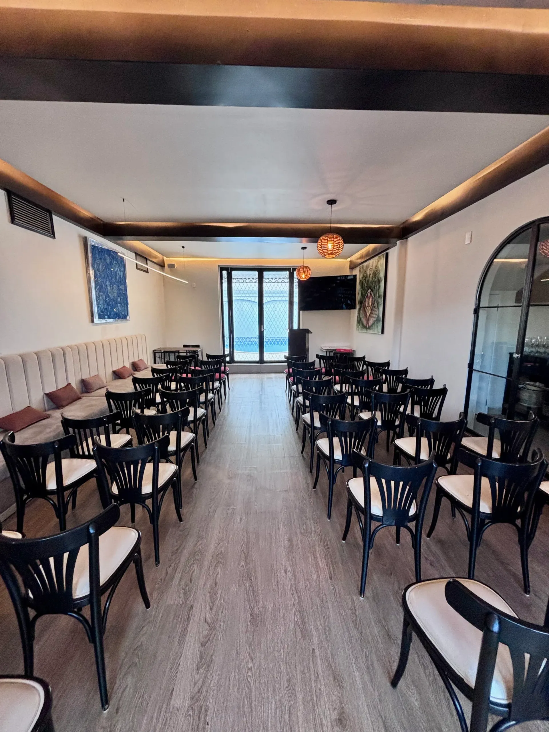 Cafetería con filas de sillas y mesas negras, interior luminoso y puertas de cristal en la parte trasera.
