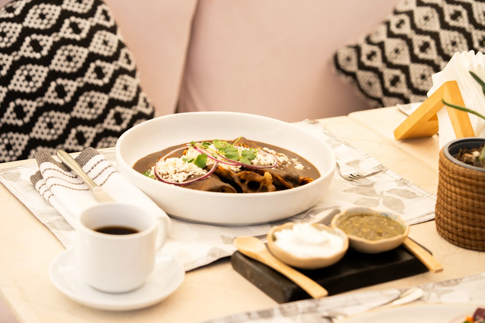 Plato japonés servido en una bandeja con sopa, arroz, té y salsas para mojar, junto a una persona con una blusa estampada.
