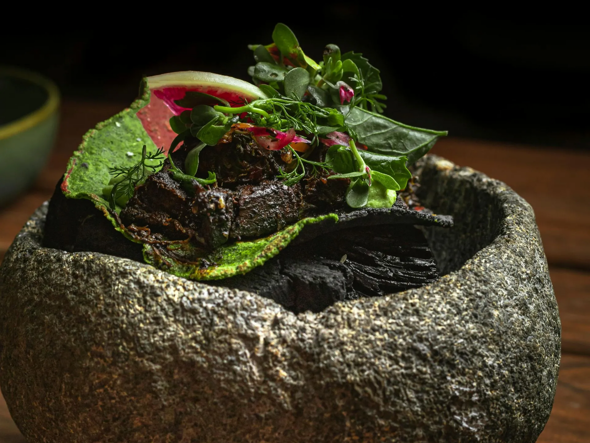 Ensalada gourmet con verduras y rábanos servida en un cuenco de piedra rústica sobre una mesa oscura.
