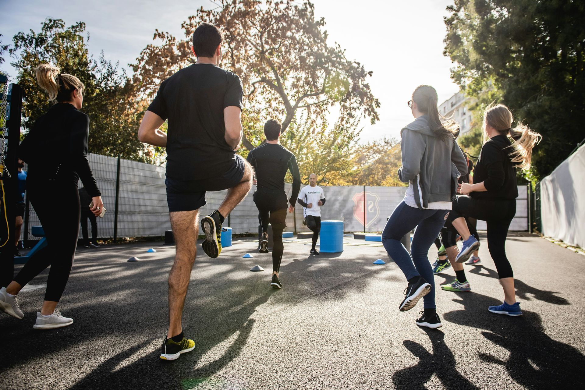 Group of people exercising outdoors, doing high knees on a paved surface. Sunny day.