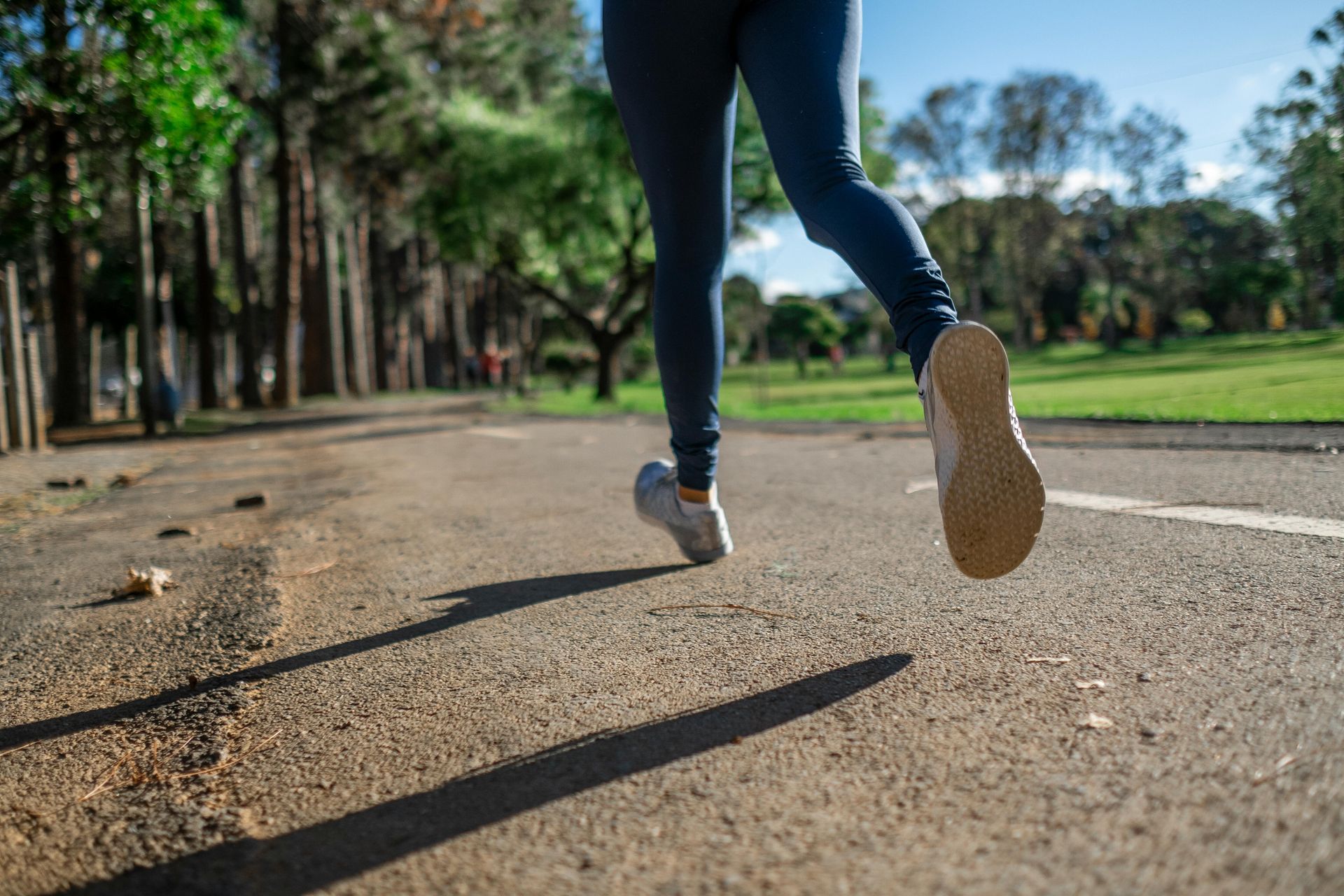 Person running on a paved path in a park; legs and shoes are in motion.